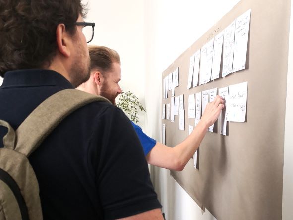 Workshop des Hyvä Camps: Teilnehmer:innen bekleben eine Pinnwand.